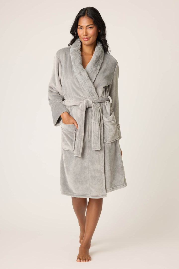 A person stands barefoot against a plain background, wearing the P.J. Salvage Luxe Plush Solid Frost Gray Robe, a light gray, knee-length fleece robe featuring a shawl collar, front pockets, and a waist tie belt.