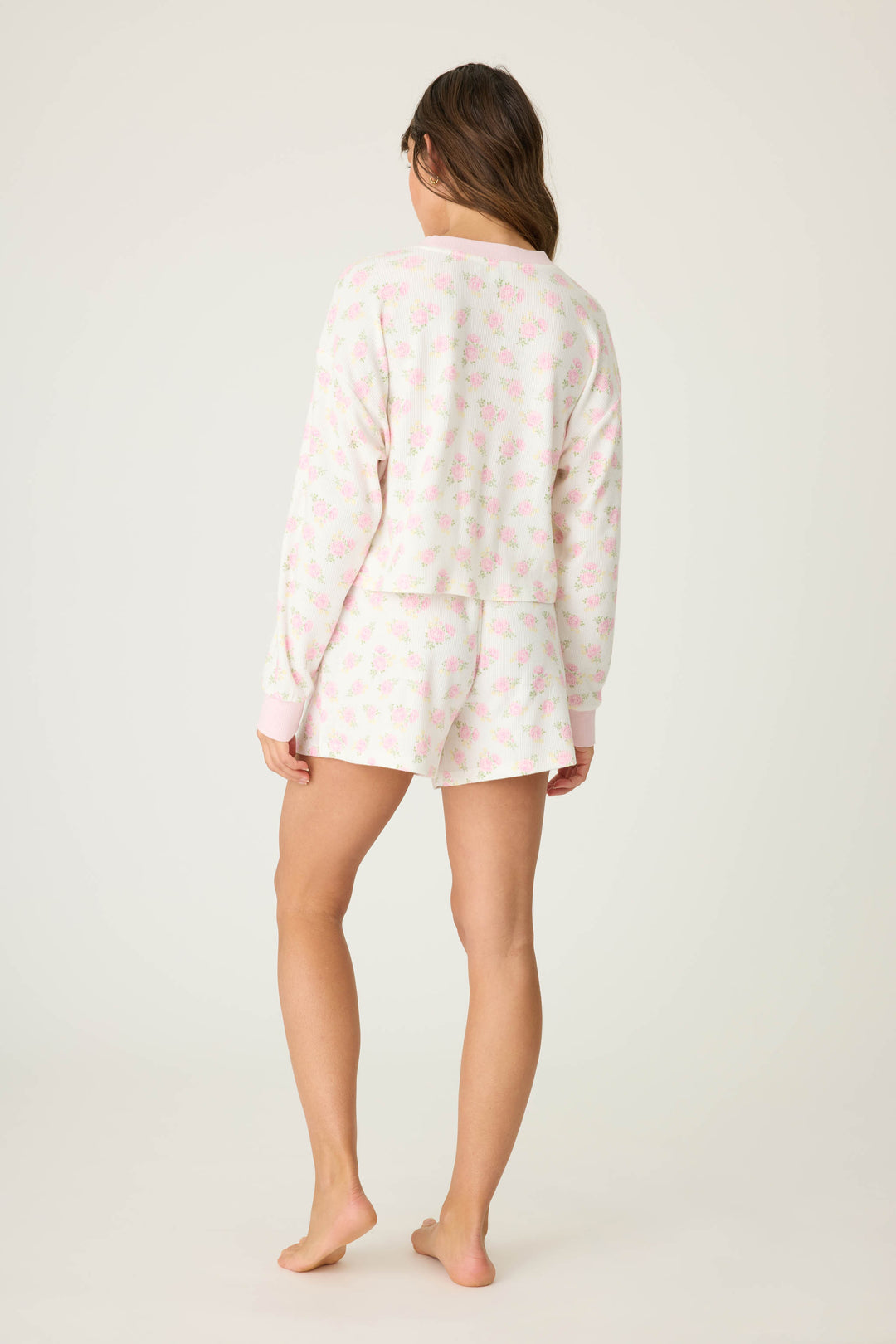 A woman stands barefoot with her back to the camera, wearing the P.J. Salvage Boyfriend Boxer Ditsy Floral Shorts Set featuring a light floral pattern on a plain background.