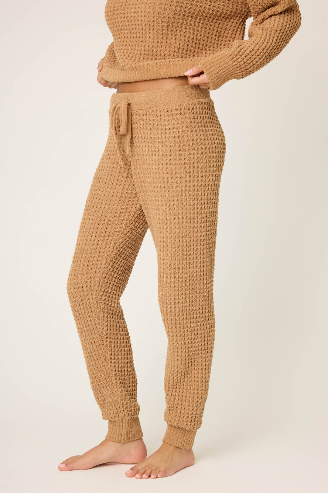 A person stands barefoot in P.J. Salvage’s Chenille Waffle Solid Caramel Banded Pant with a drawstring waist and matching top. The image is cropped at the shoulders against a plain light beige background.