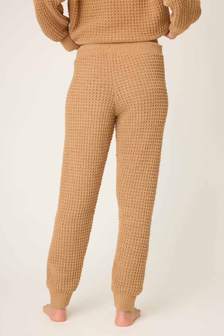 Person stands barefoot, facing away from the camera, wearing P.J. Salvage's Chenille Waffle Solid Caramel Banded Pant and matching top against a plain, light background.