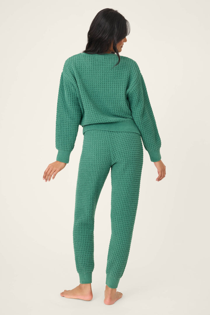 A person with long dark hair stands barefoot facing away, wearing the P.J. Salvage Chenille Waffle Solid Forest Lounge Set against a plain light background.