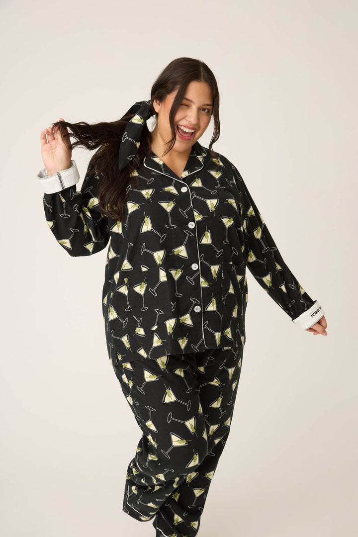 A smiling person with long dark hair poses against a plain background, wearing the Merrier With A Martini Flannel Plus Size PJ Set by P.J. Salvage and holding a section of their hair with one hand.