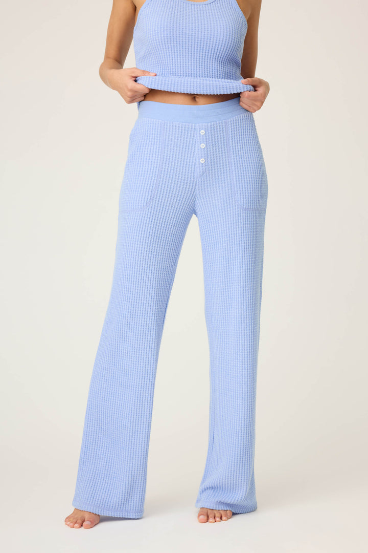 A person models the P.J. Salvage Morning Waffles Solid Peri Open Leg Pant—light blue, high-waisted knit pants with buttons and front pockets—paired with a matching sleeveless top, standing barefoot against a plain background, face not visible.