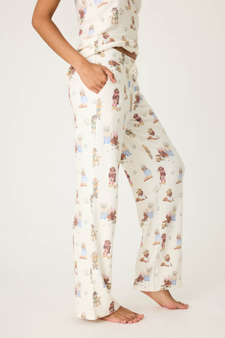A person stands barefoot wearing P.J. Salvage DOGS OPEN LEG PANT RUFF ON THE RANGE pajama pants, featuring a drawstring waist and an allover dog print. Only the lower torso and legs are visible against a plain background.
