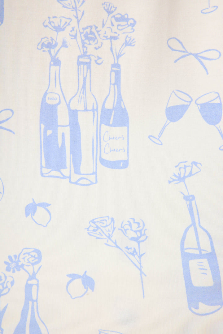 The Parisian Dreams Whimsical Print PJ Set by P.J. Salvage features a white background with light blue illustrations of wine bottles (one labeled Cheers Cheers), wine glasses, bows, lemons, and flowers.