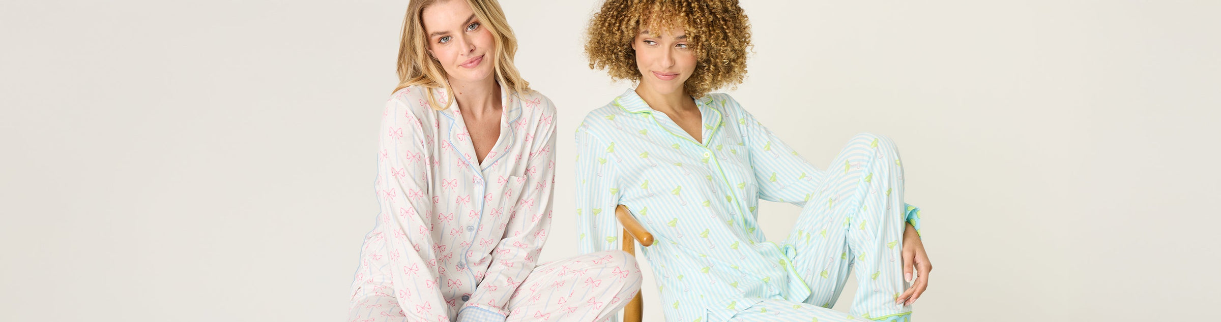 Four women stand in a row, each wearing a colorful t-shirt with graphic prints and text. The shirts are pink, blue, and green, featuring designs like sunsets, cocktails, and bold lettering.