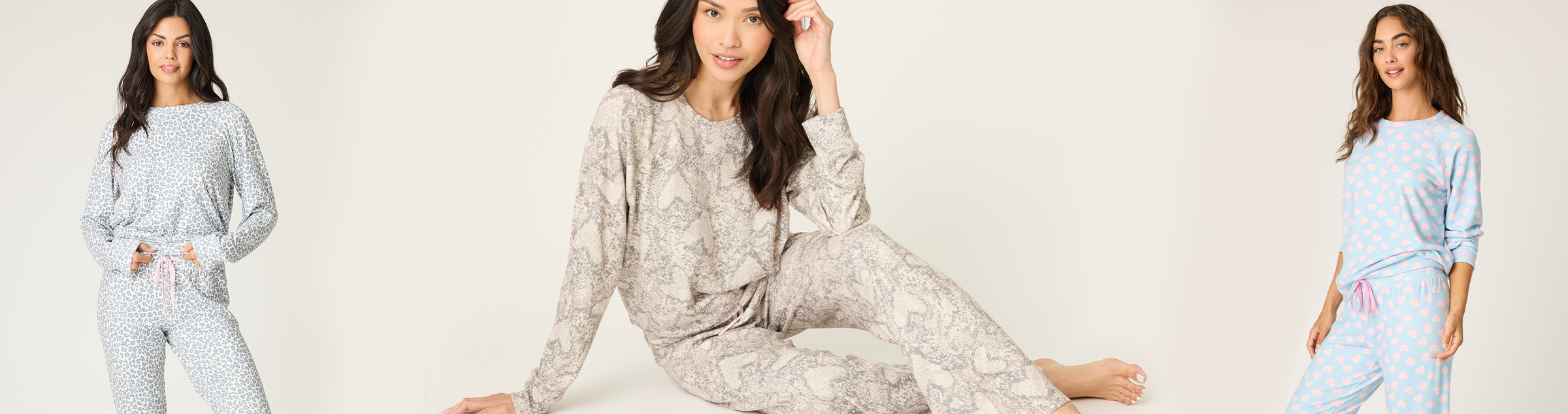 A woman models different sets of pajamas: drinking from a mug, sitting cross-legged in grey printed pajamas, and standing in a white top and pink bottoms, all against a plain light background.