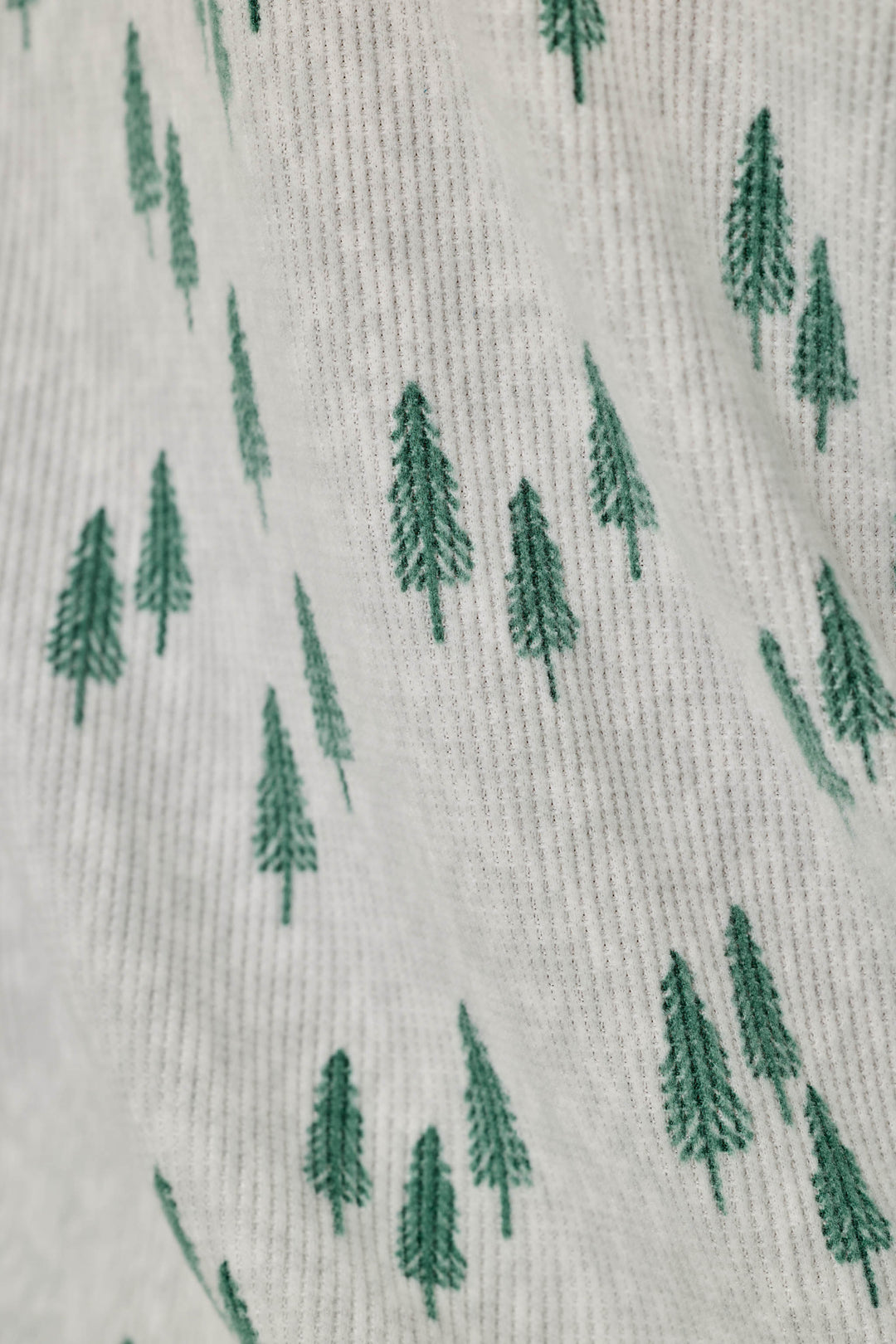 Close-up of a knit fabric with a repeating pattern of small green pine trees on a light off-white background.