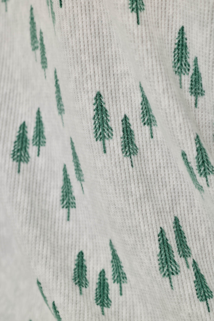 Close-up of a knit fabric with a repeating pattern of small green pine trees on a light off-white background.