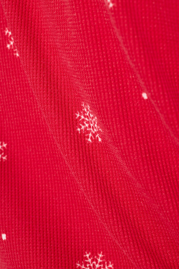 A close-up of a bright red knit fabric with small white snowflake patterns scattered across it.