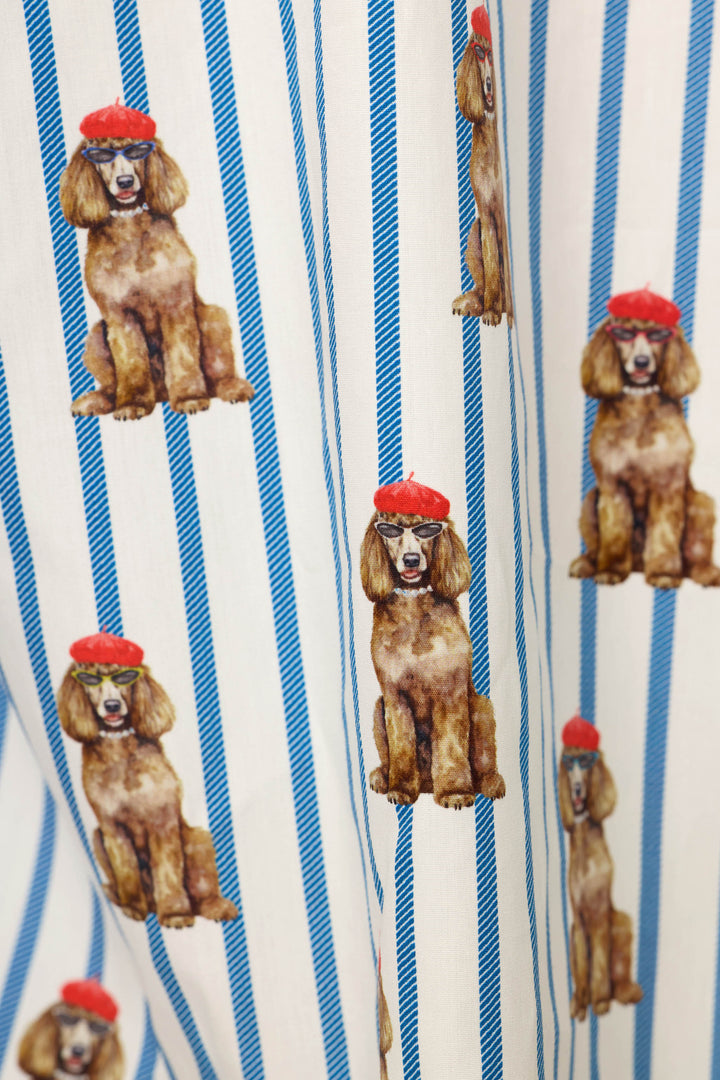 A close-up of a printed fabric featuring brown poodle illustrations wearing red berets over a white background with vertical blue stripes.