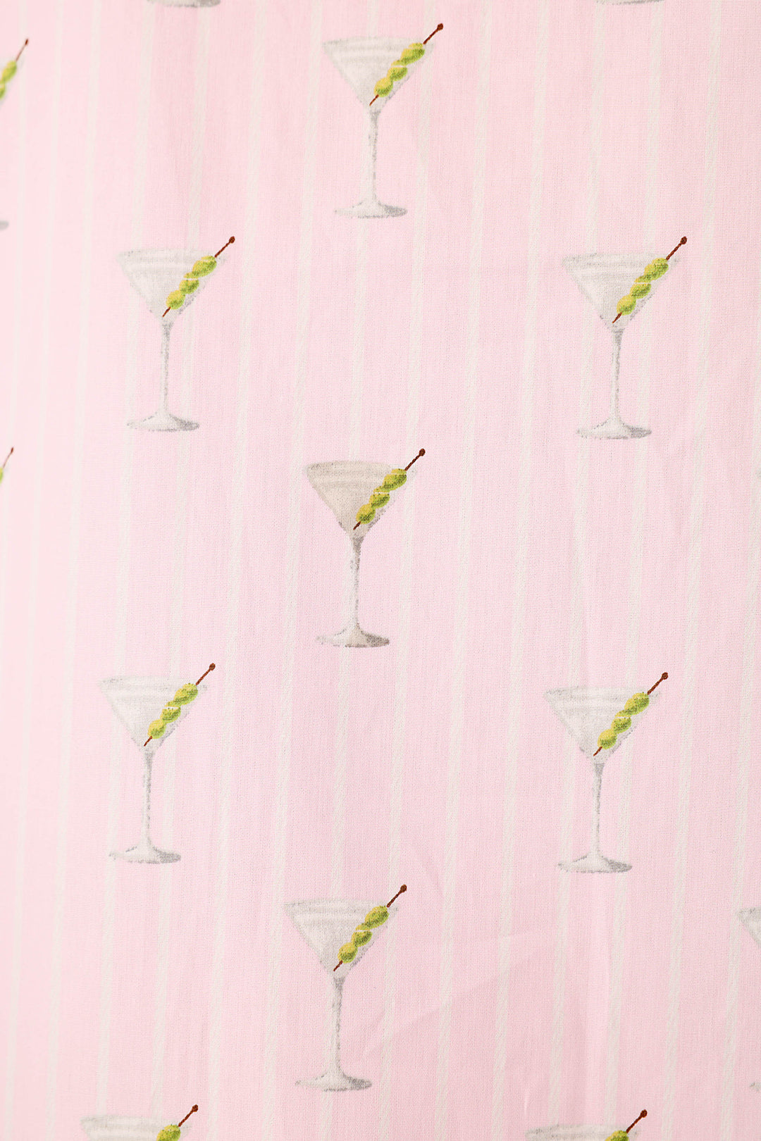 Close up of a pink and white striped fabric with a repeating pattern of martini glasses with 3 green olives.