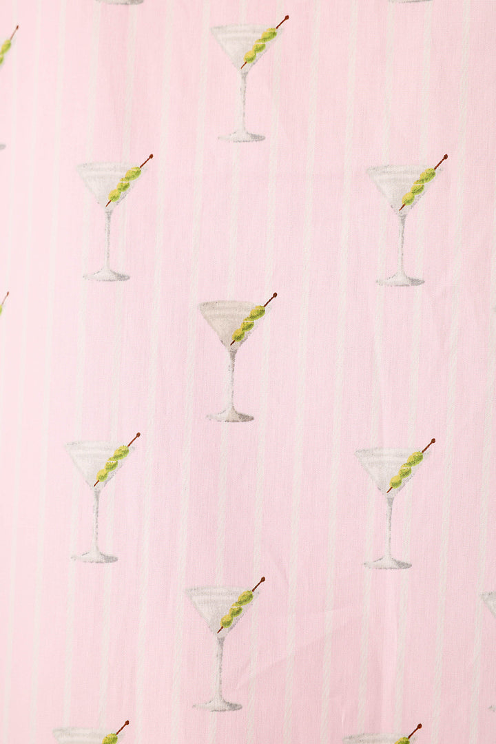 Close up of a pink and white striped fabric with a repeating pattern of martini glasses with 3 green olives.