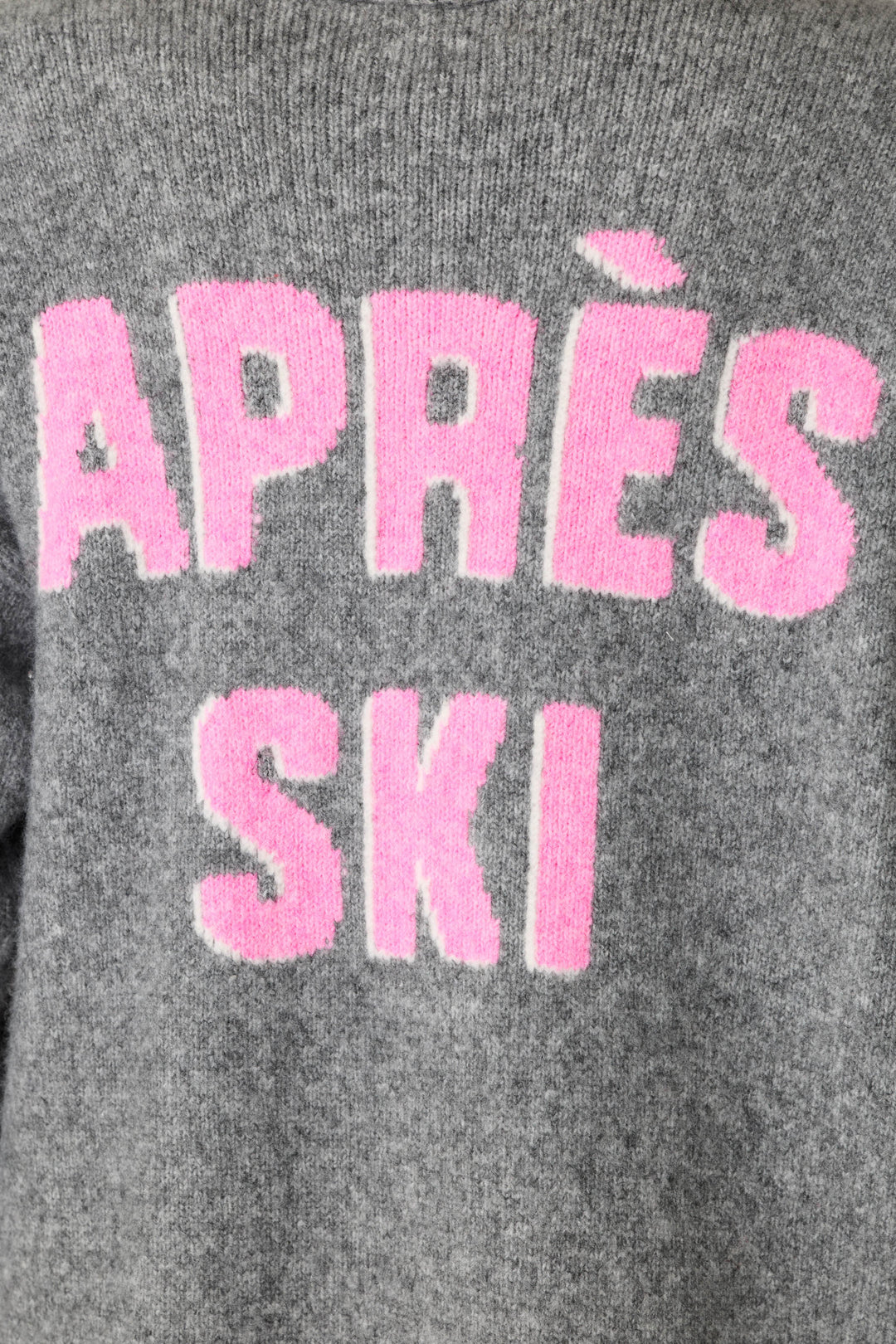 Close-up of a gray knit sweater with large pink fuzzy text reading 'APRÈS SKI' in all caps across the back.