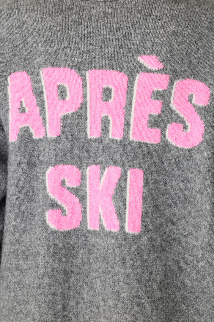 Close-up of a gray knit sweater with large pink fuzzy text reading 'APRÈS SKI' in all caps across the back.