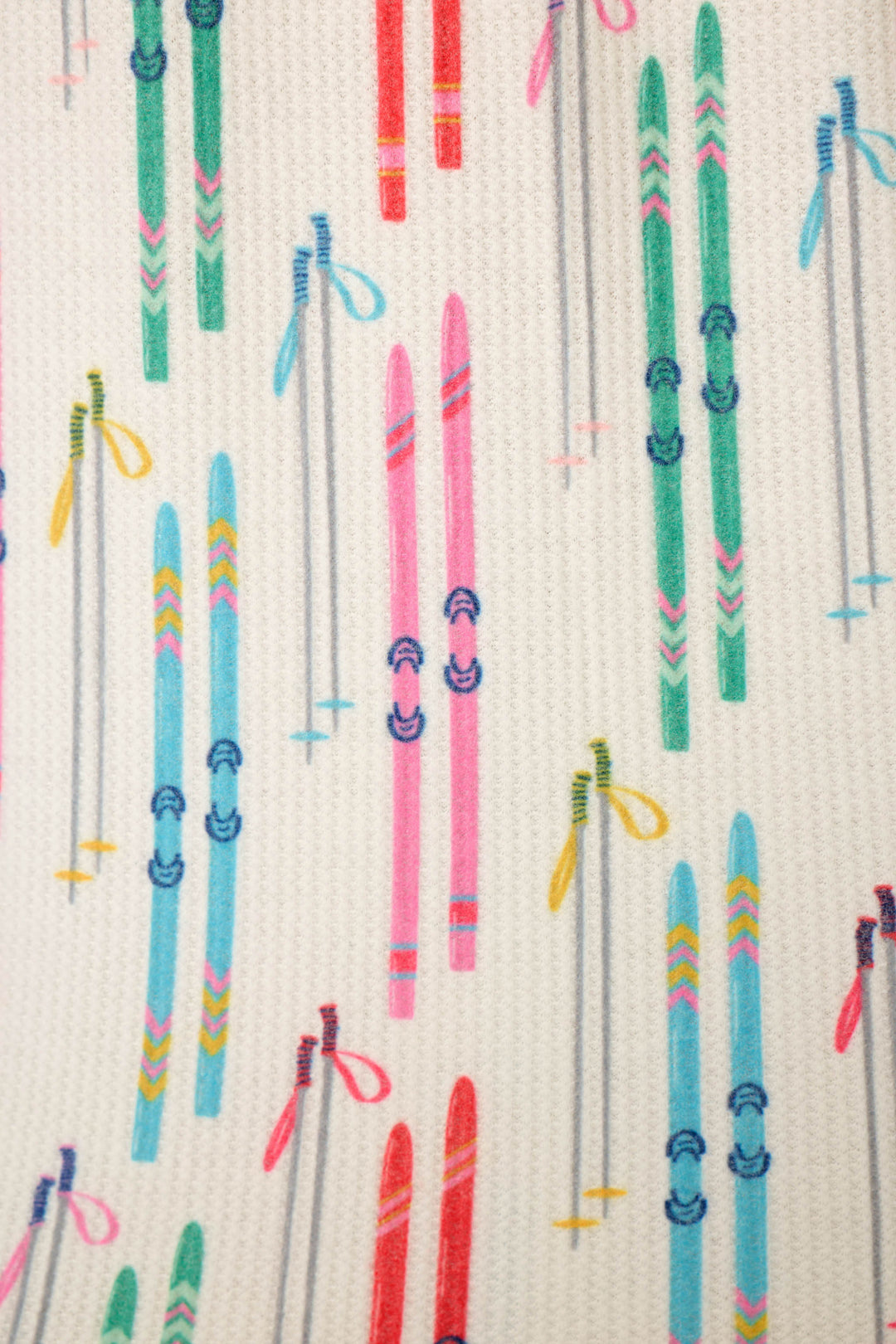 A close-up of fabric featuring colorful skis and ski poles printed on a small, waffle-textured off-white background.