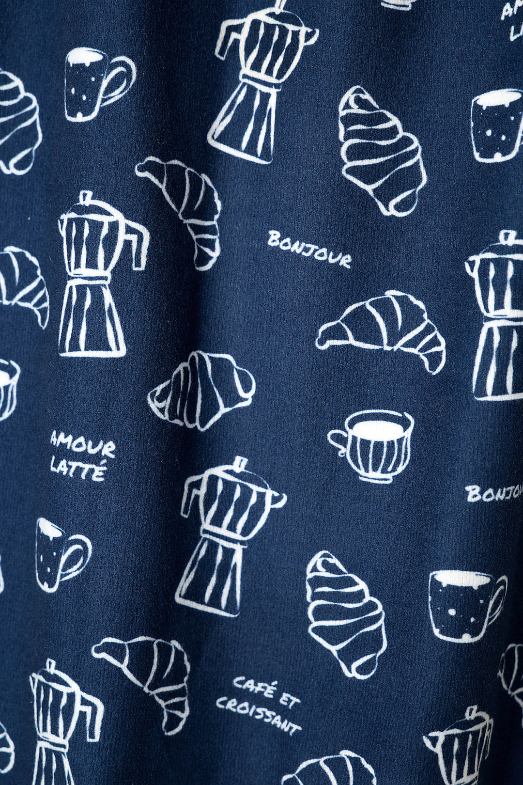 A close-up of a navy fabric with a white, hand-drawn style print of coffee mugs, croissants, metal stovetop espresso makers, and French phrases including 'BONJOUR' and 'AMOUR LATTE'.
