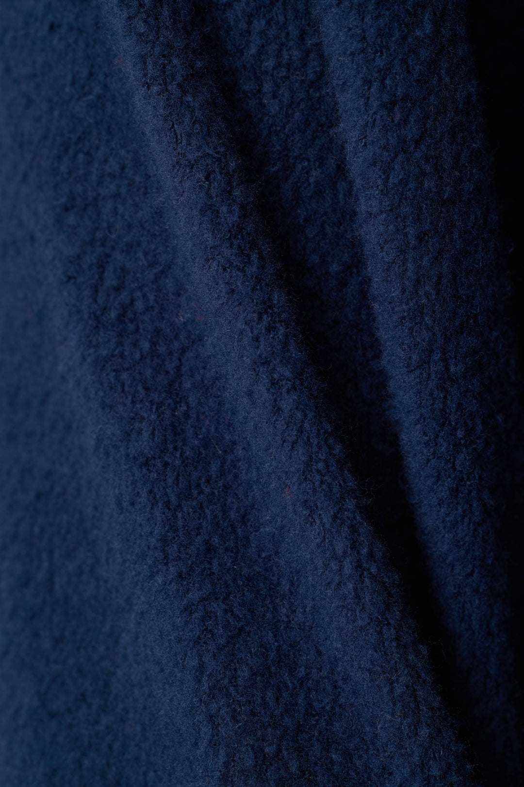 A close-up of dark navy blue textured fabric with soft folds and a plush, looped surface.