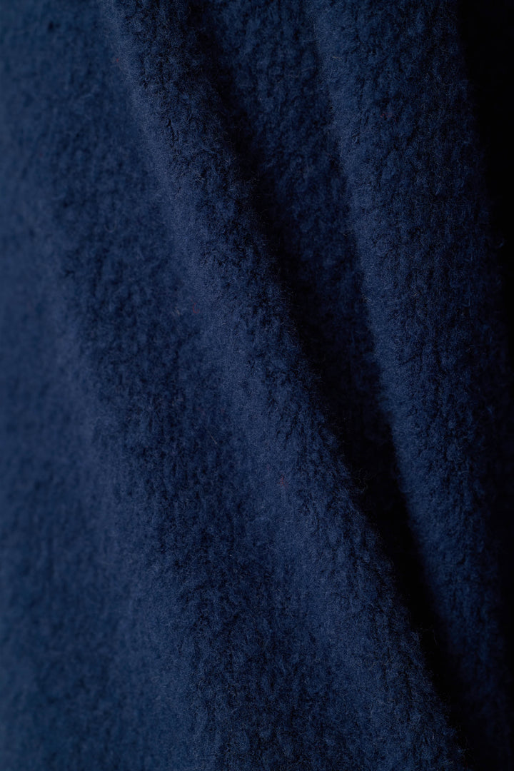A close-up of dark navy blue textured fabric with soft folds and a plush, looped surface.