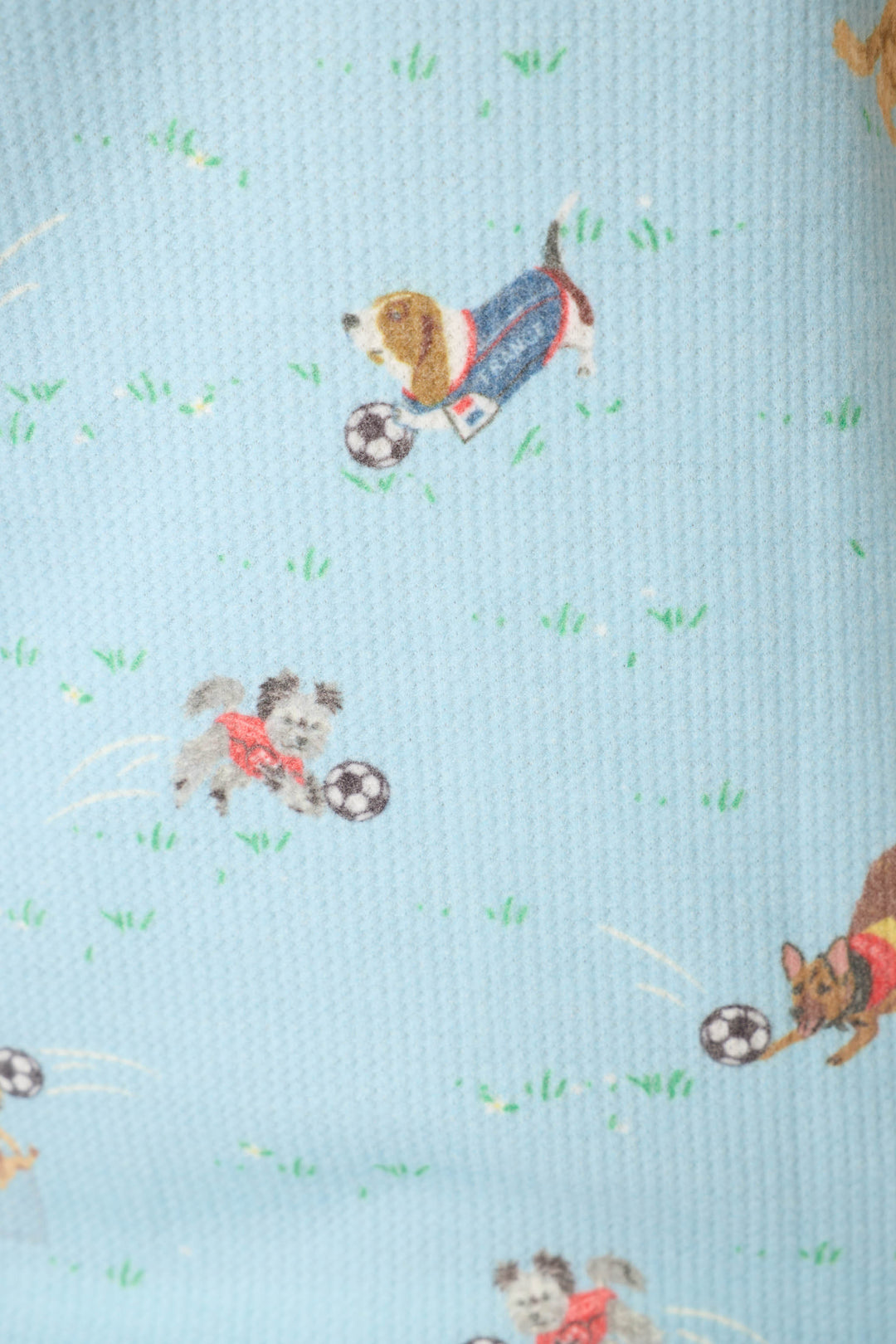 Blue fabric with a playful pattern of pups in outfits, soccer balls, and grassy fields.