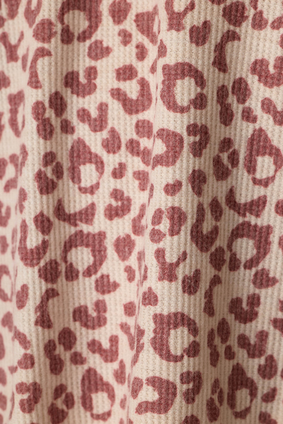 Close-up of a waffle-textured fabric with an allover leopard print pattern in dusty wine on a warm beige background.