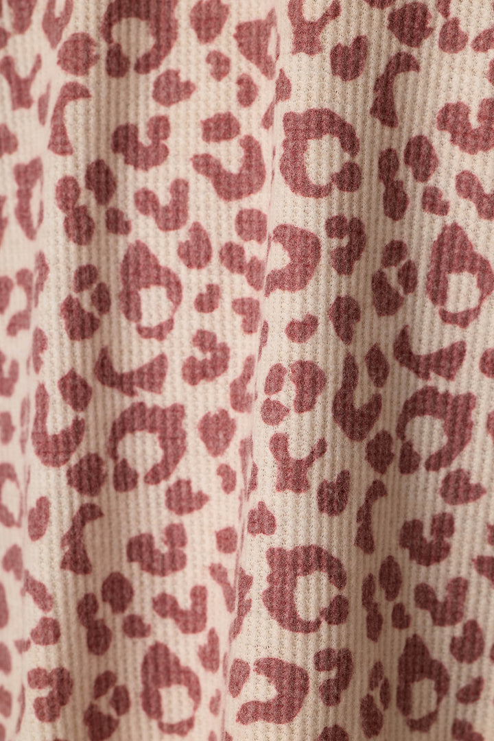 Close-up of a waffle-textured fabric with an allover leopard print pattern in dusty wine on a warm beige background.