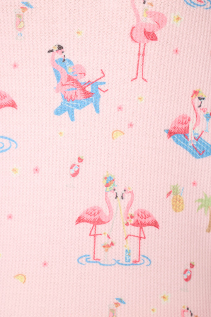 Pink fabric featuring cartoon flamingos, women in swimsuits, and scattered tropical motifs like pineapples and lemons.