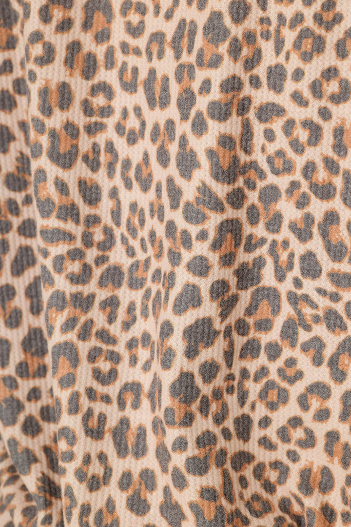 Close-up of a leopard print fabric with a beige base, brown spots, and dark gray to black outlines.