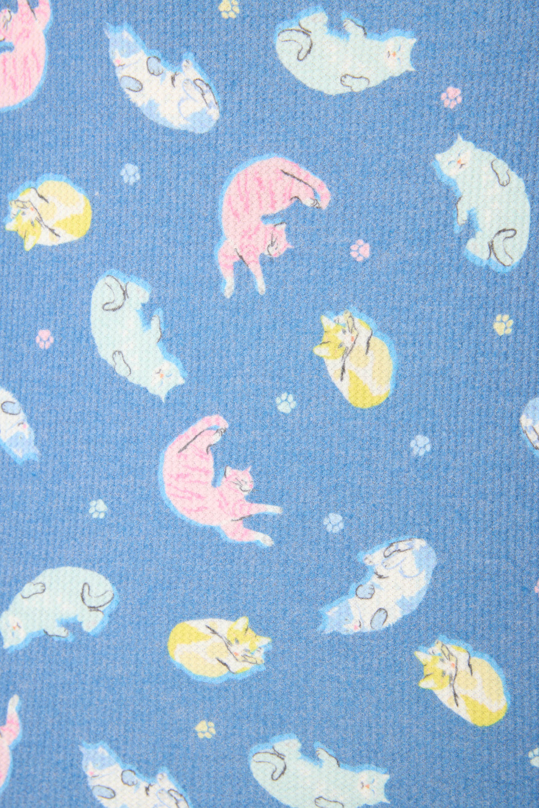 The fabric is blue with playful cartoon cats in yellow, pink, and white, along with pastel paw prints scattered throughout.