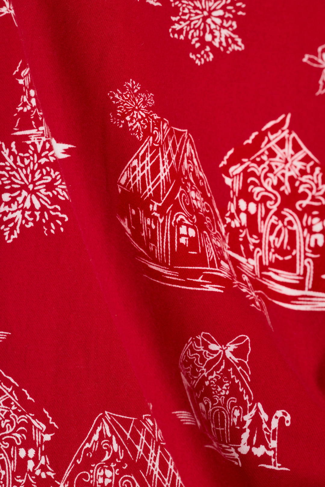 Red fabric with a white printed pattern of gingerbread houses, candy canes, and snowflakes.