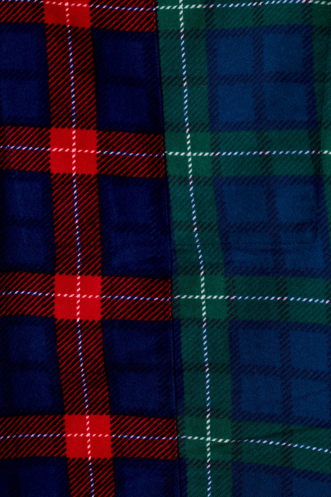 Close-up of tartan fabric showing two plaid sections: one in navy blue with red and white stripes, and one in dark green with blue and white stripes.