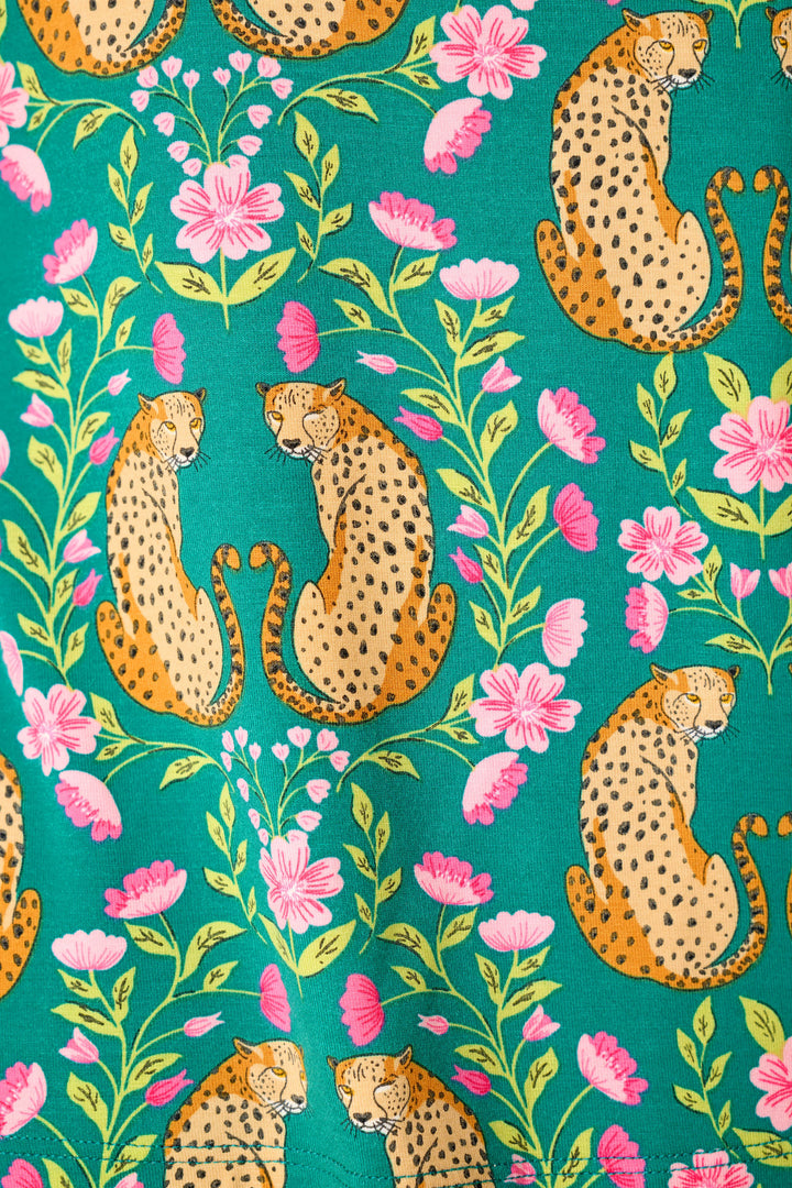 Cheetahs with black spots sit gracefully among pink flowers and green leaves in a repeating pattern on a bright teal background.