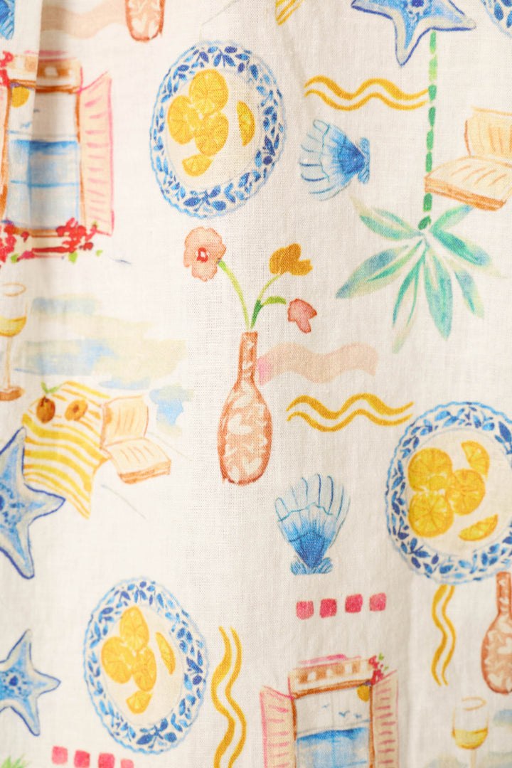 White fabric with a vibrant print of plates, lemons, seashells, flowers in vases, starfish, palm leaves, books, and wine glasses.