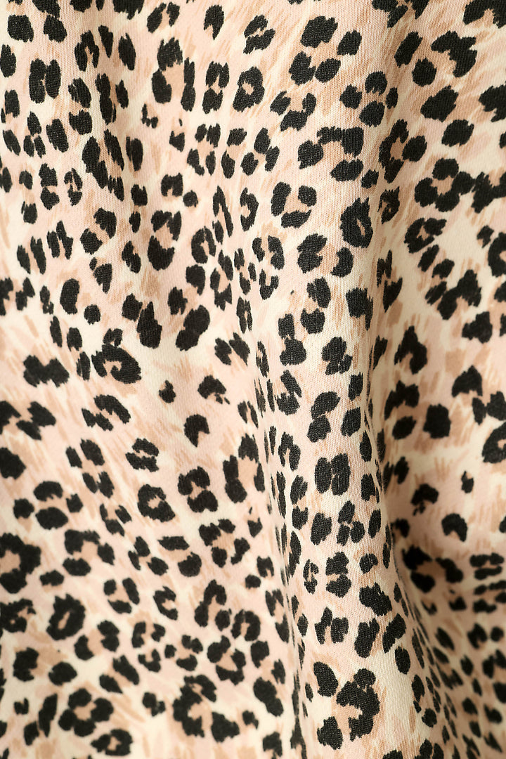 Close-up of a leopard print fabric with black irregular spots on a light beige background.