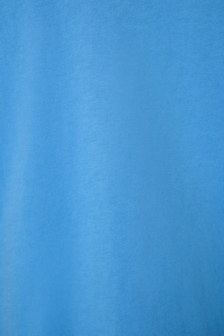 A close-up of a solid medium blue fabric texture with subtle vertical folds.