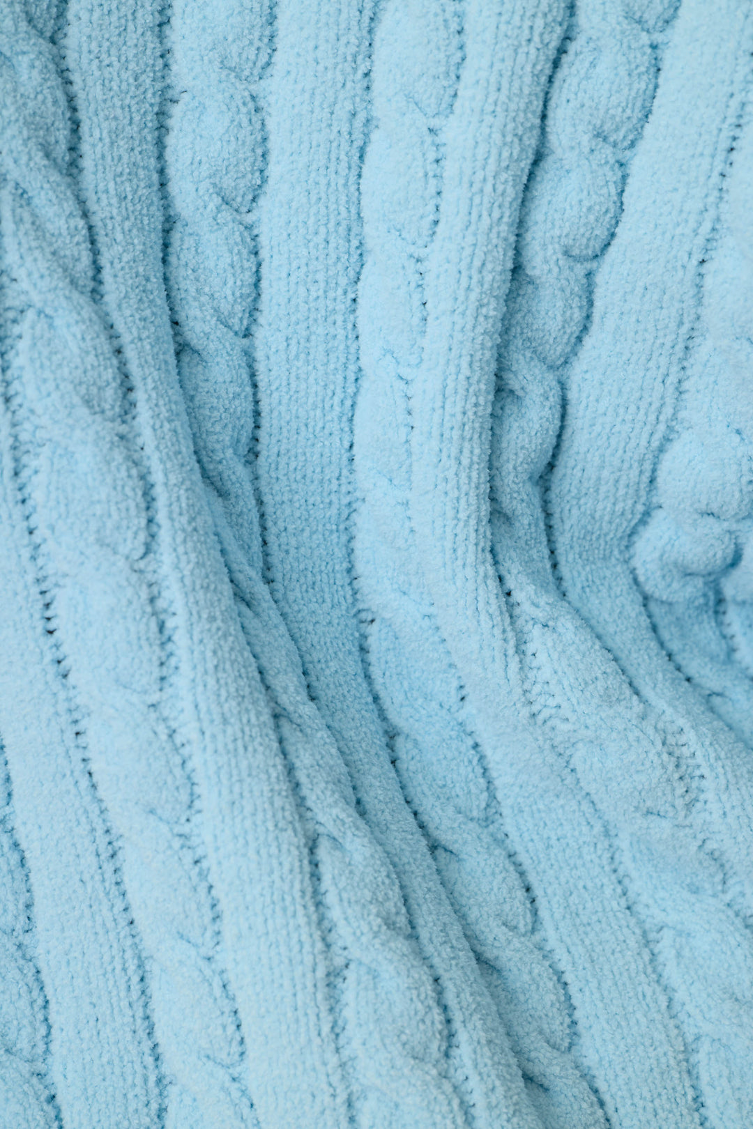 A close-up of a light blue cable-knit fabric texture, showing the detailed knit pattern and soft folds.