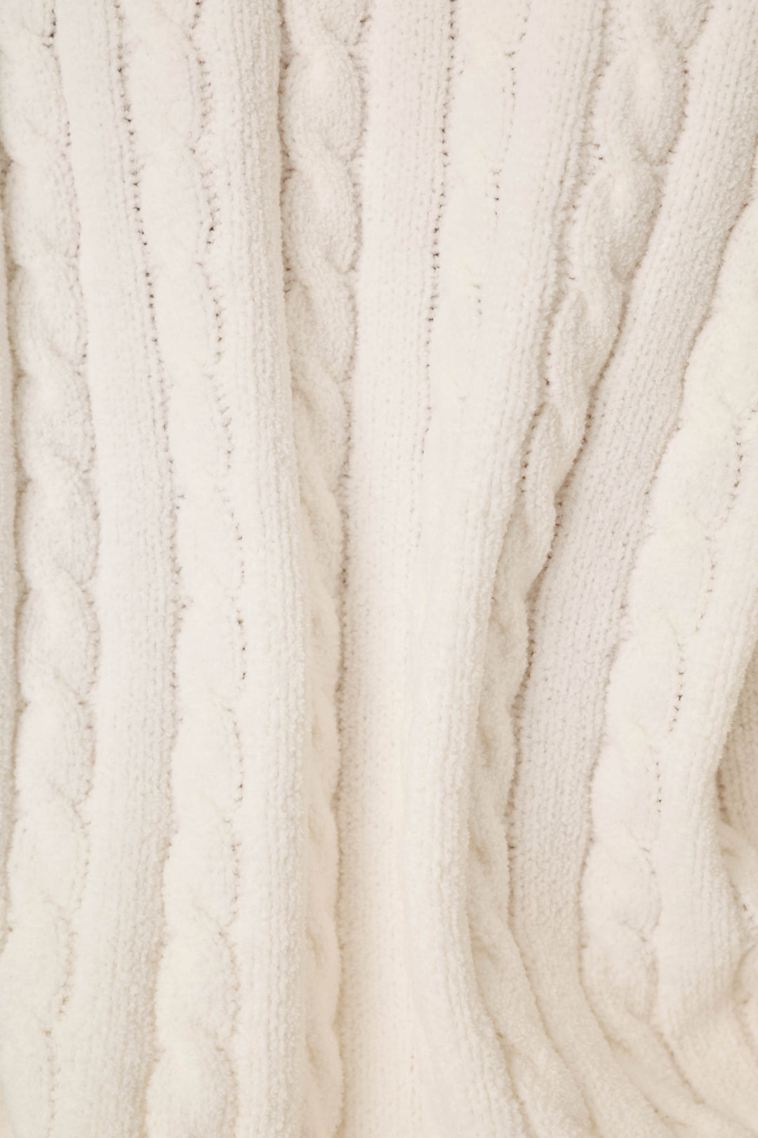 Close-up of a cream-colored cable-knit fabric texture, showing the detailed knit pattern and soft folds.