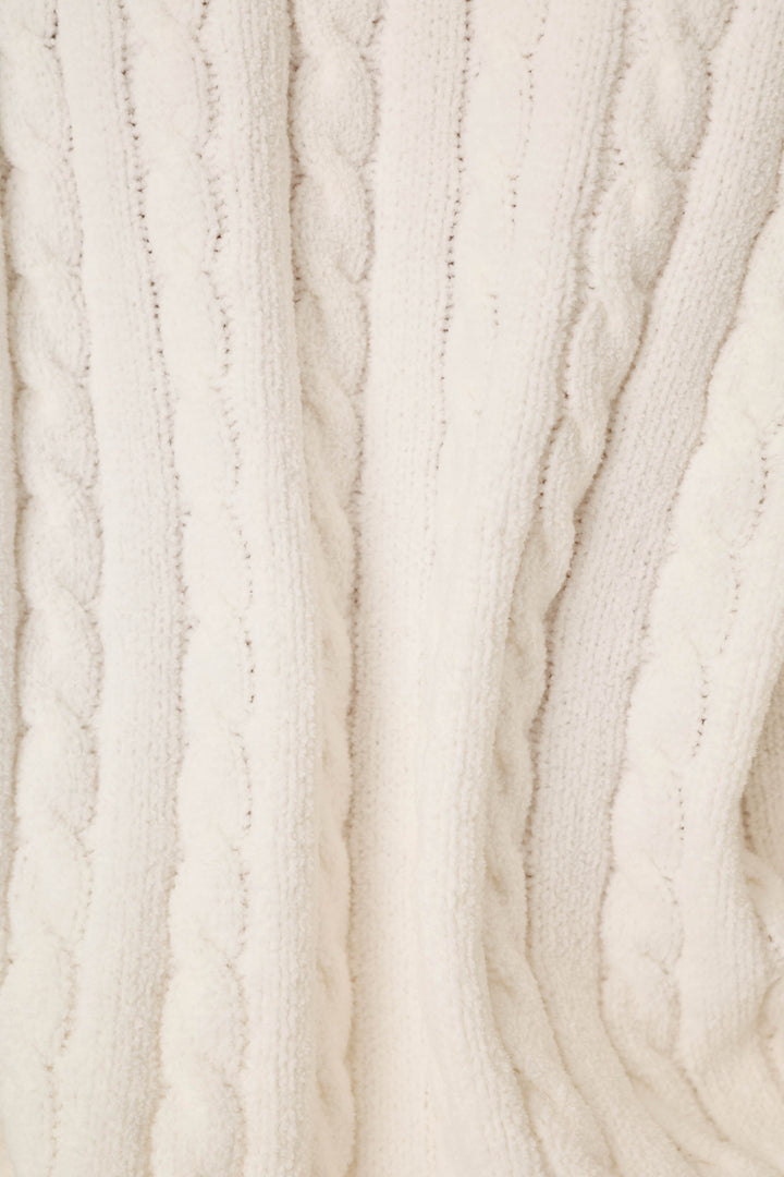 Close-up of a cream-colored cable-knit fabric texture, showing the detailed knit pattern and soft folds.