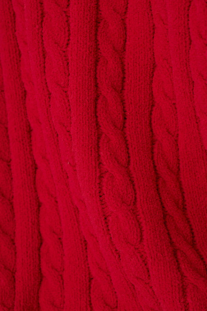A close-up of a bright red cable-knit fabric texture, showing the detailed vertical cable pattern.