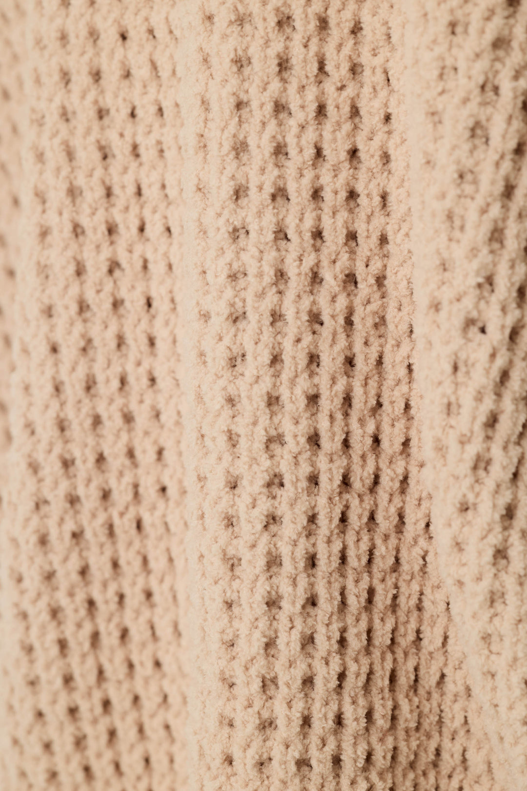 Close-up of a beige knit fabric with a textured waffle pattern.