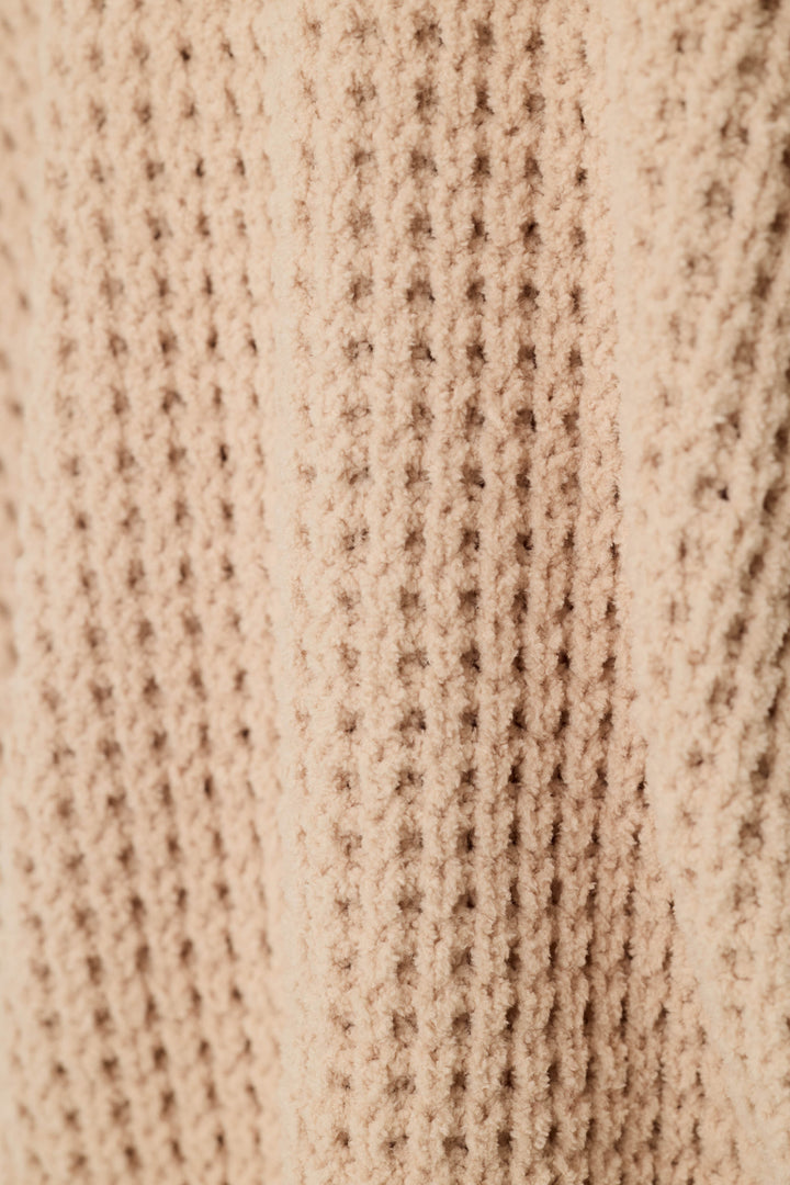 Close-up of a beige knit fabric with a textured waffle pattern.