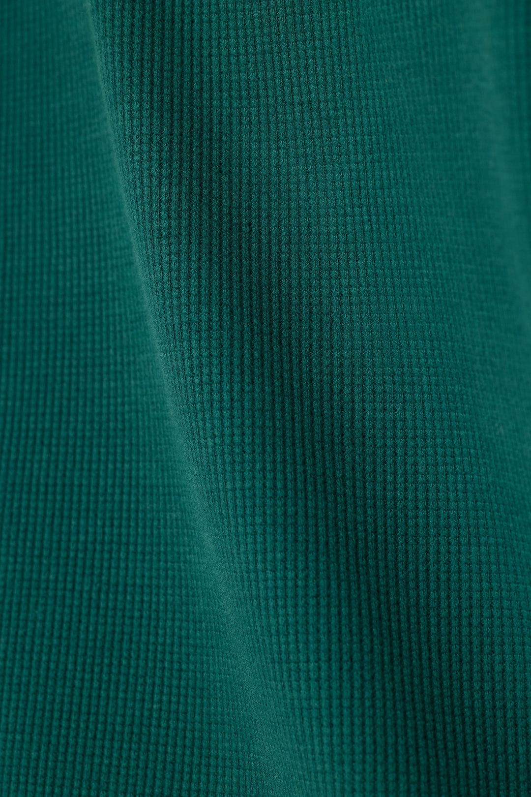 A close-up of a dark teal green waffle fabric texture with soft folds.