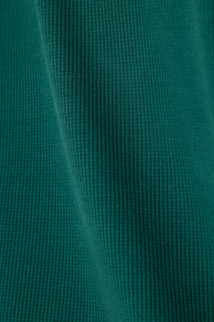A close-up of a dark teal green waffle fabric texture with soft folds.