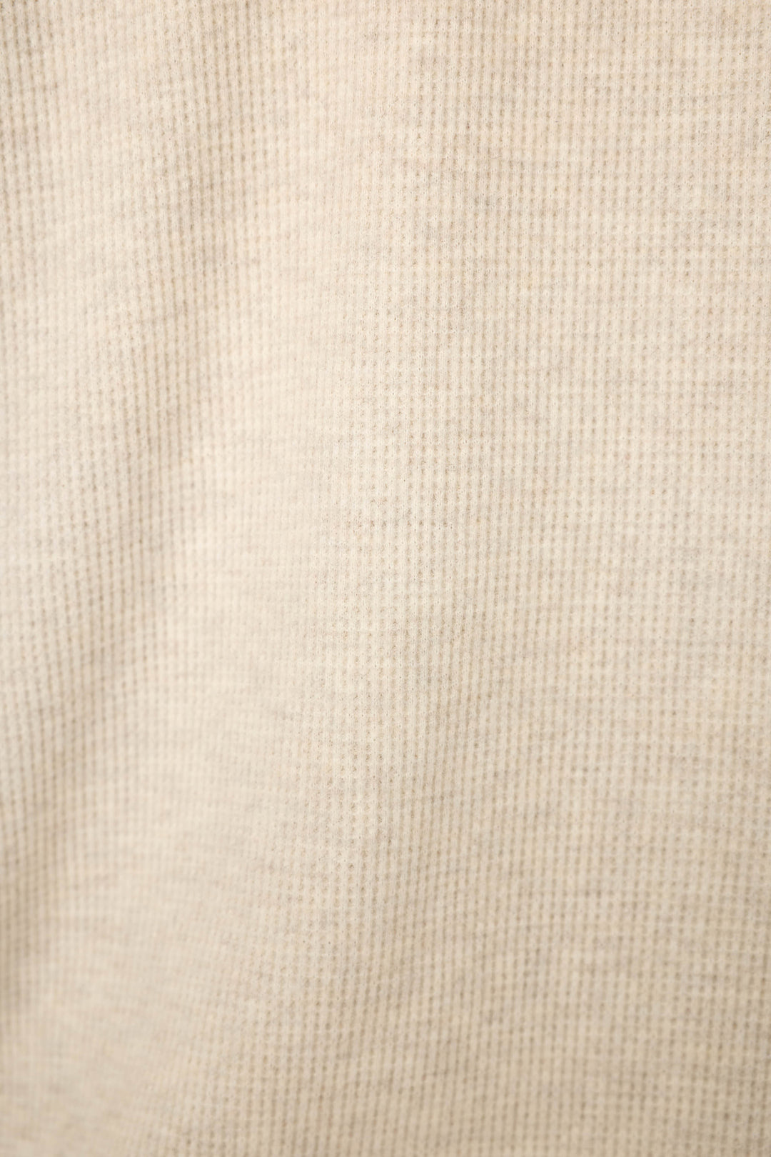 A close-up of a soft natural color knit fabric with a waffle texture.