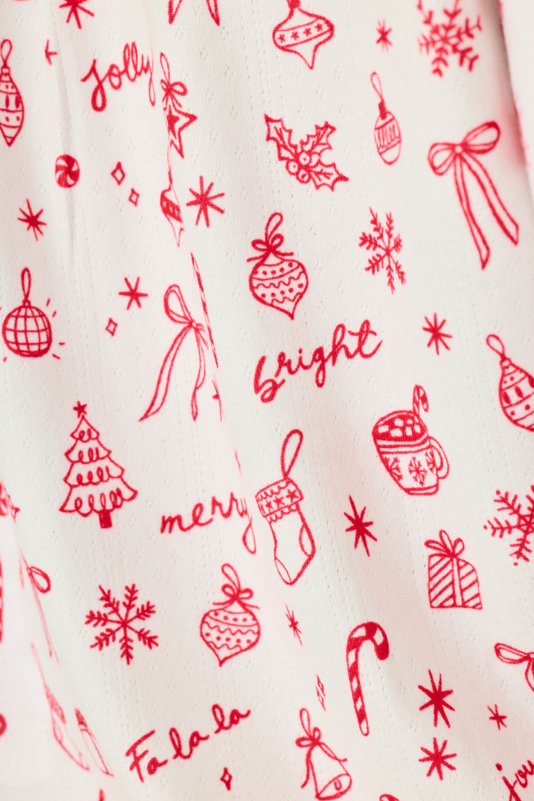 Close-up of a white fabric with a red Christmas-themed print featuring ornaments, bows, snowflakes, candy canes, stockings, mugs, and festive words like 'jolly', 'bright', and 'merry'.