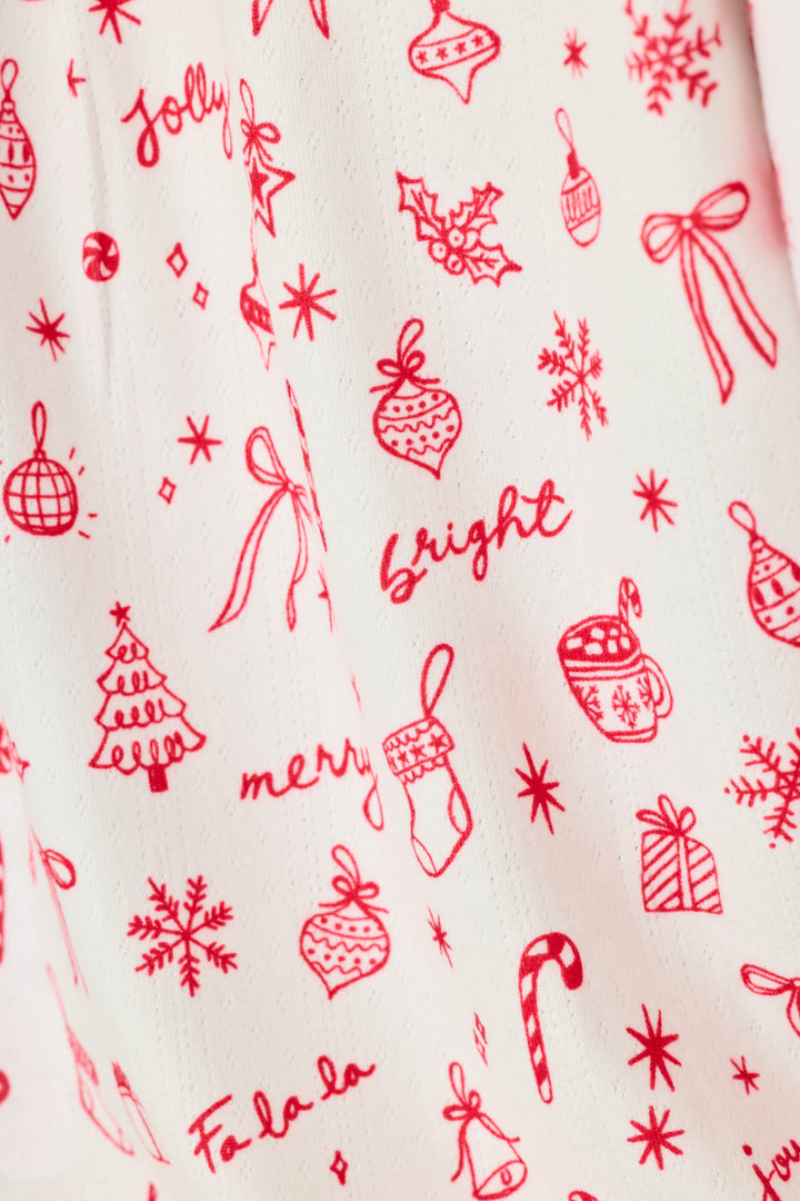 Close-up of a white fabric with a red Christmas-themed print featuring ornaments, bows, snowflakes, candy canes, stockings, mugs, and festive words like 'jolly', 'bright', and 'merry'.