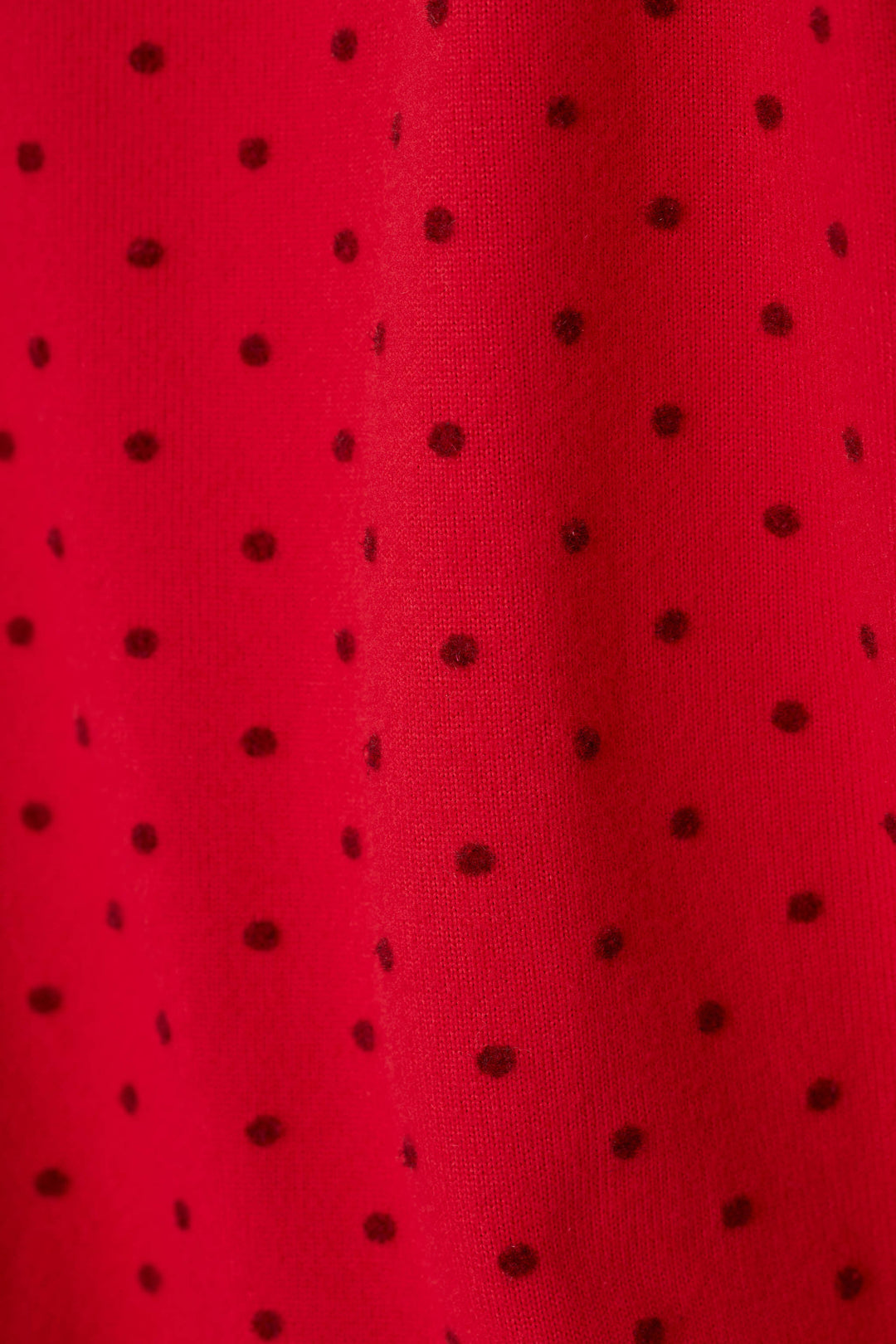 A close-up of a bright red fabric with a repeating pattern of small tonal polka dots, showing a soft vertical fold in the center.