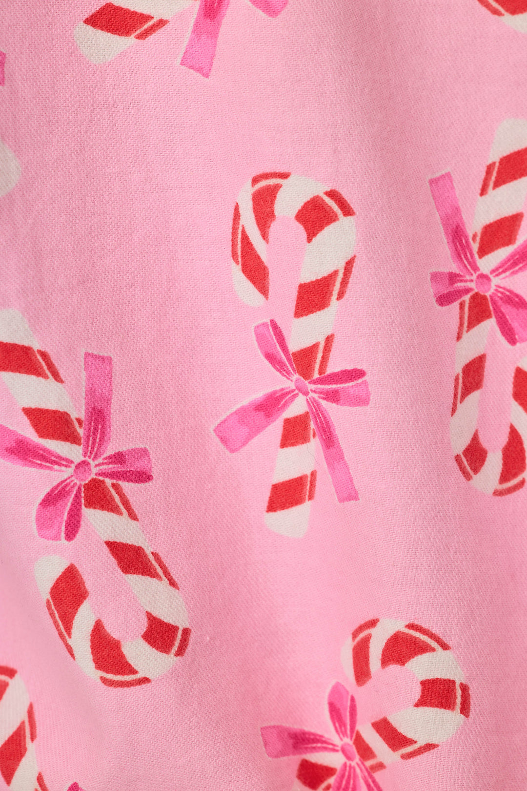 A close-up of a pink fabric with a repeating pattern of red and white striped candy canes tied with pink bows.