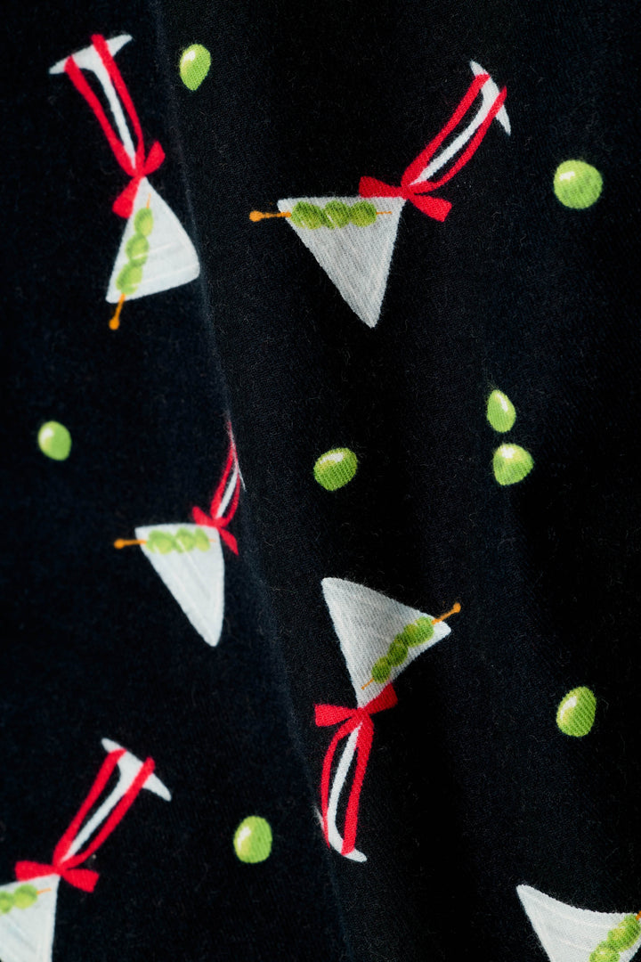 Close-up of a black fabric with a repeating pattern of white martini glasses filled with 3 green olives on s stick, bows around the stems, and scattered green olives throughout the fabric.