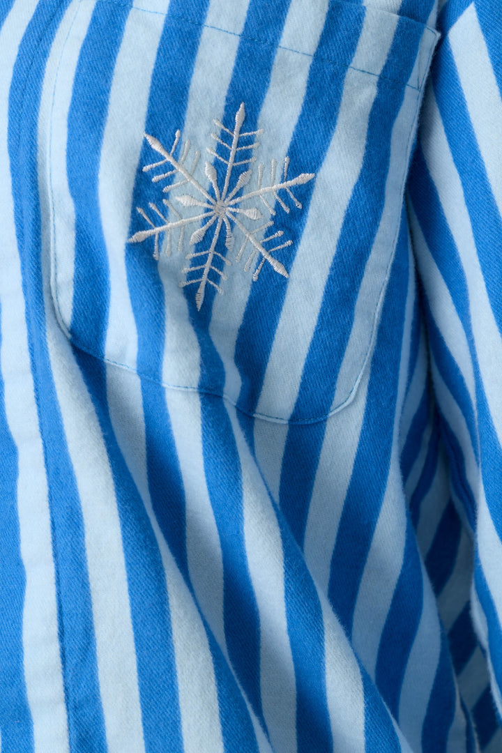 A close-up of the P.J. Salvage Snowflake Icon 3-Piece Long Sleeve Flannel PJ Set fabric, featuring blue and light blue vertical stripes and a white embroidered snowflake on the chest pocket.